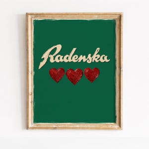 以下が含まれることがあります： 緑色の背景に、筆記体で「Radenska」の文字と3つの赤いハートが描かれた額入りのアートプリント。 フレームは薄茶色です。