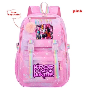 May include: Pink K-Pop themed backpack with a graphic of three figures and the text "KPOP DEMON HUNTERS." The backpack has rainbow accents, a fluffy keychain, and the word "pink" in the upper right corner.