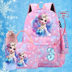 May include: A pink Frozen-themed backpack set featuring Elsa. The set includes a backpack, lunch bag, water bottle, and pencil case. The backpack has a large image of Elsa and the number 3. The set is decorated with stars and snowflakes.