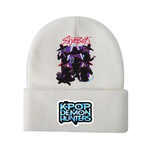 Könnte beinhalten: Weißer Beanie mit einer Grafik von Figuren in schwarzen Hüten und dem Text "SAJABOYS" in Lila und Rot. Darunter ein Quadrat mit dem Text "KPOP DEMON HUNTERS" in Blau und Grün.