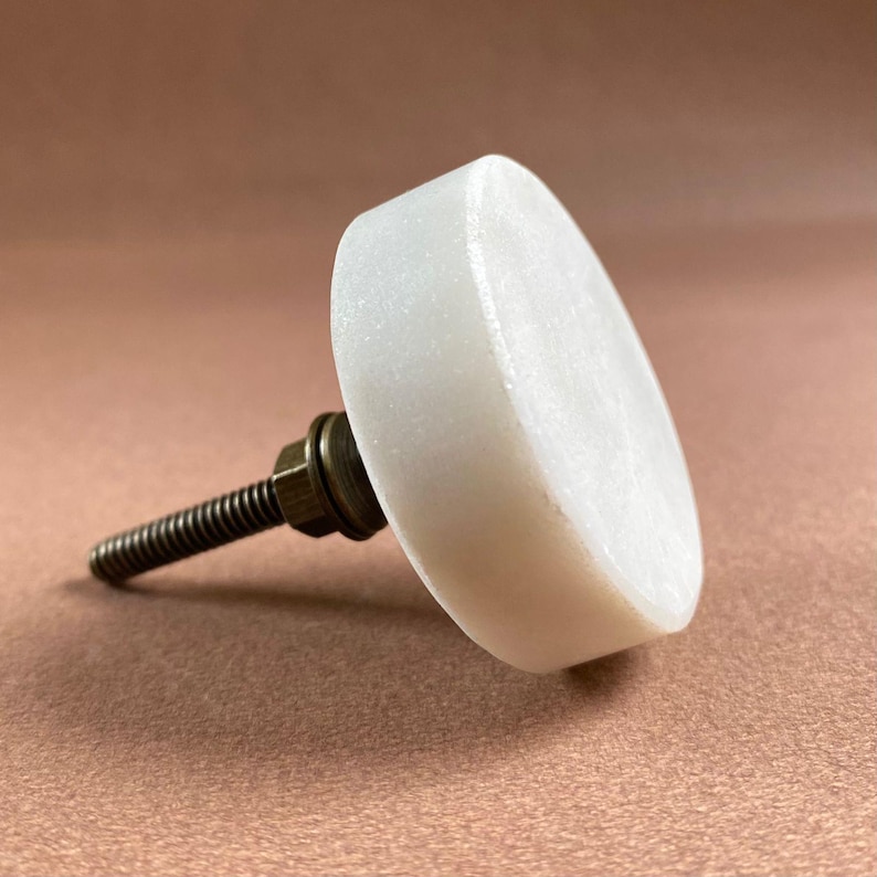 Pode incluir: Um puxador de arm&aacute;rio de m&aacute;rmore branco com parafuso e porca de lat&atilde;o. O puxador redondo tem uma superf&iacute;cie ligeiramente texturizada. O hardware foi projetado para f&aacute;cil instala&ccedil;&atilde;o e adiciona um toque de eleg&acirc;ncia a qualquer m&oacute;vel.