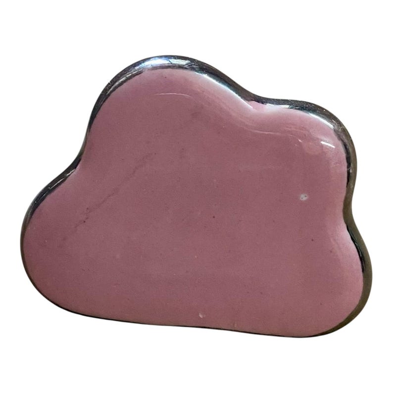 May include: A pink, cloud-shaped gua sha tool with a silver trim. The smooth, polished surface reflects light, highlighting the tool's rounded edges and overall shape. This facial massage tool is designed for skincare routines.