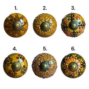 May include: A selection of six decorative cabinet knobs. Each knob has a unique design in shades of yellow, with red, pink, and black accents. The knobs have a brass-coloured base.