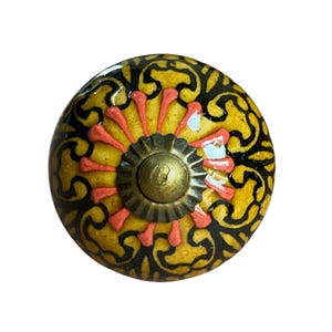 May include: A decorative cabinet knob with a yellow, black, and coral design. The knob features a floral pattern and a brass-coloured centre. This unique hardware adds a touch of elegance to any furniture piece.