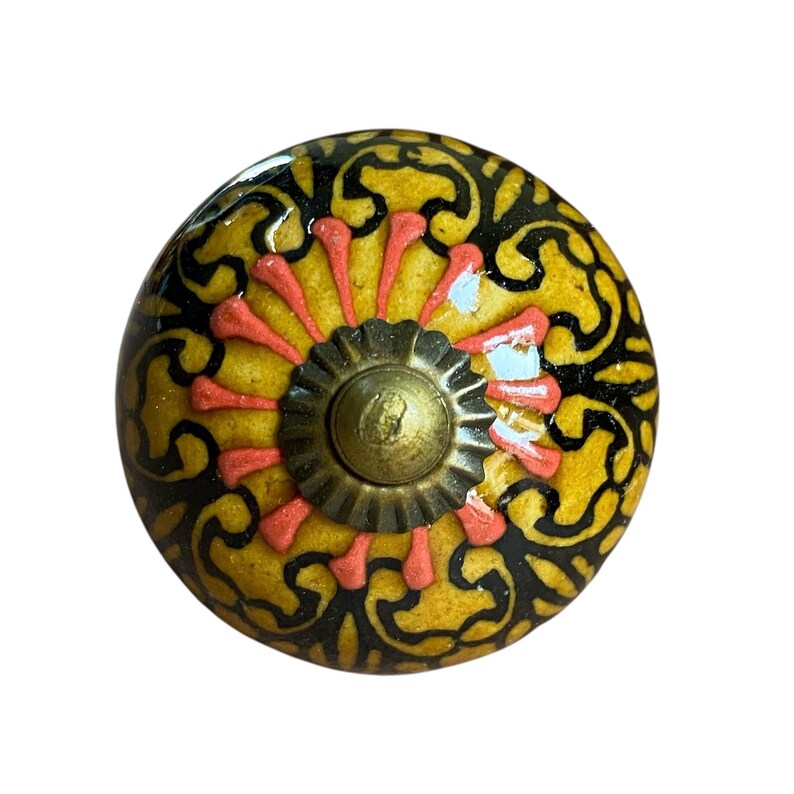 May include: A decorative cabinet knob with a yellow, black, and coral design. The knob features a floral pattern and a brass-coloured centre. This unique hardware adds a touch of elegance to any furniture piece.