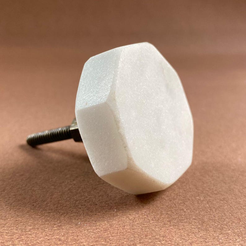 Pode incluir: Um puxador de arm&aacute;rio de m&aacute;rmore branco com um design geom&eacute;trico facetado. O puxador tem formato hexagonal e &eacute; preso a um parafuso de metal rosqueado. Este hardware decorativo &eacute; adequado para gavetas e arm&aacute;rios.