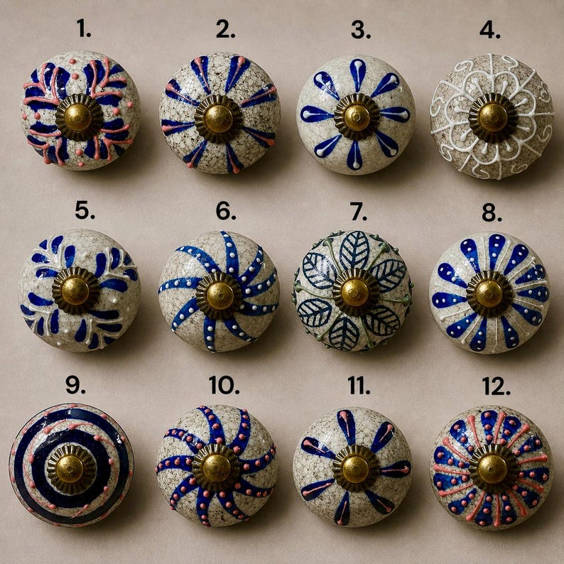 Op de afbeelding: Een verzameling van twaalf decoratieve keramische kastknoppen. Elke knop heeft een uniek ontwerp met verschillende kleuren, waaronder blauw, roze, wit en groen. De knoppen hebben een messingkleurige metalen basis.