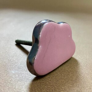 May include: A heart-shaped cabinet knob with a dark grey, glossy border and a light pink centre. The threaded bolt is made of metal. Suitable for drawers or cupboards.