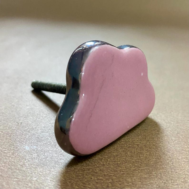 May include: A heart-shaped cabinet knob with a dark grey, glossy border and a light pink centre. The threaded bolt is made of metal. Suitable for drawers or cupboards.