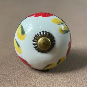 Puede incluir: Pomo de cer&aacute;mica para armario con base blanca, adornado con motivos florales rojos y amarillos. El pomo presenta una base met&aacute;lica de color lat&oacute;n y un tornillo central. Esta ferreter&iacute;a decorativa a&ntilde;ade un toque de color y estilo.