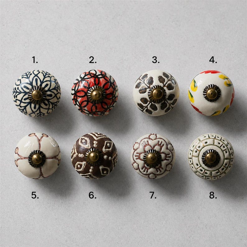 Puede incluir: Ocho pomos de cer&aacute;mica decorativos con varios dise&ntilde;os florales y geom&eacute;tricos. Los pomos presentan colores como blanco, negro, rojo, marr&oacute;n y amarillo, con herrajes color lat&oacute;n. Cada pomo est&aacute; numerado para facilitar la selecci&oacute;n.