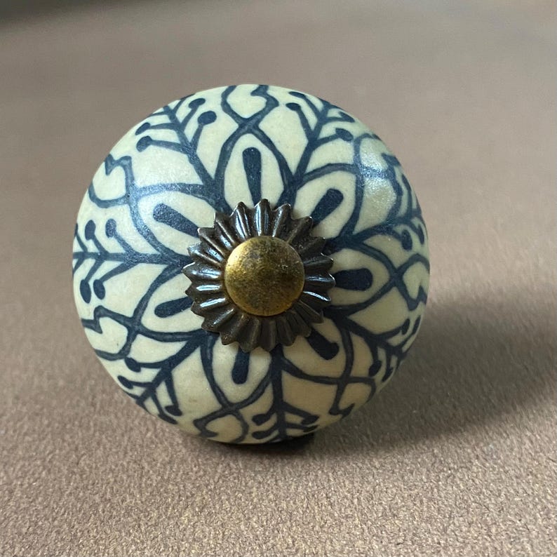 Puede incluir: Pomo decorativo para armario con base color crema y un estampado floral azul oscuro. El pomo presenta un centro en forma de estrella de color bronce. Adecuado para cajones y armarios. Di&aacute;metro aproximado de 4 cm.