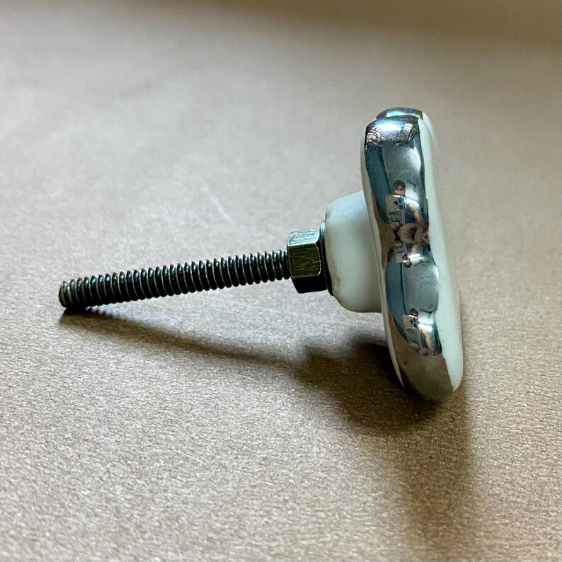 May include: A white and silver cabinet knob with a floral design. The knob has a silver trim and a threaded rod for installation. The hardware is designed for use on drawers, cabinets, or furniture.