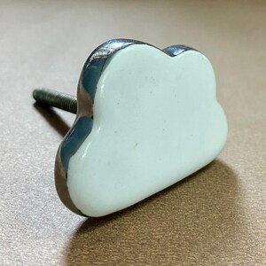 May include: A cloud-shaped cabinet knob with a white centre and a shiny, silver-coloured border. The knob has a threaded metal post for attachment. The hardware is designed for use on drawers, cabinets, or furniture.