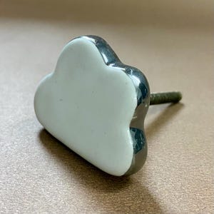 May include: A cloud-shaped cabinet knob with a white centre and a shiny, silver-coloured trim. The knob has a threaded screw for easy installation. This decorative hardware adds a whimsical touch to furniture.