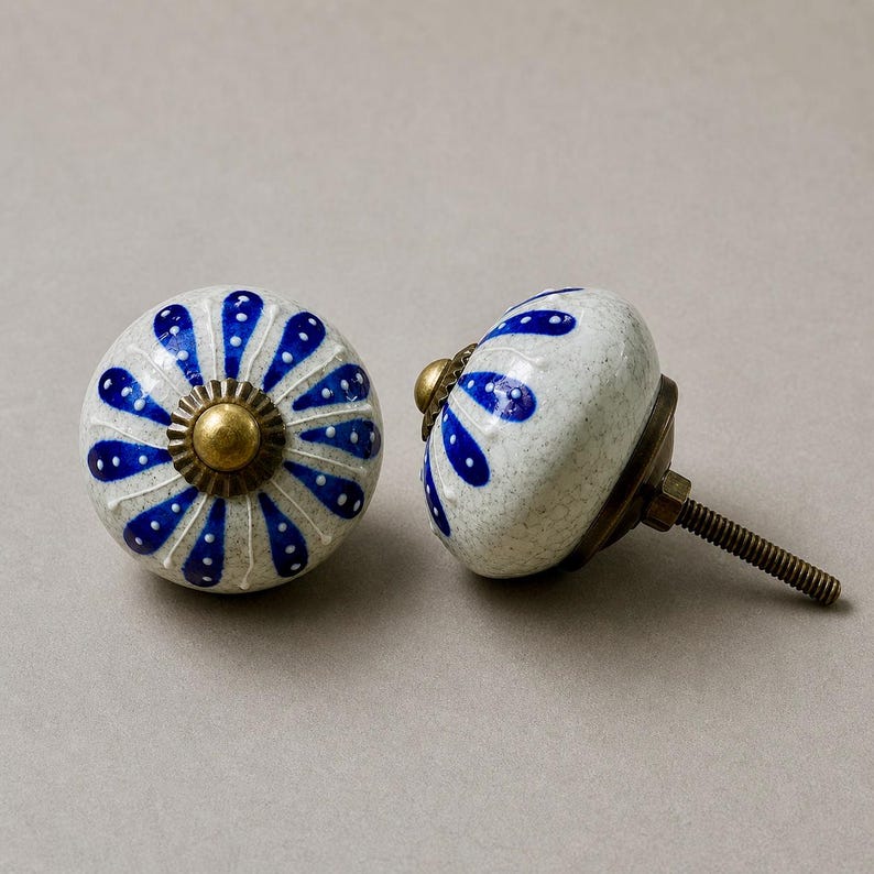 Op de afbeelding: Twee keramische kastknoppen met een witte basis en een blauw bloemmotief. De knoppen hebben een messingkleurige basis en schroef. De knoppen zijn decoratief en kunnen worden gebruikt voor laden of kasten.