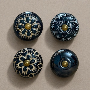 Puede incluir: Cuatro pomos de cerámica azul oscuro con herrajes dorados. Dos pomos presentan un diseño floral dorado, uno tiene un diseño floral blanco y uno es liso. Estos pomos decorativos son ideales para añadir un toque de elegancia a los muebles.