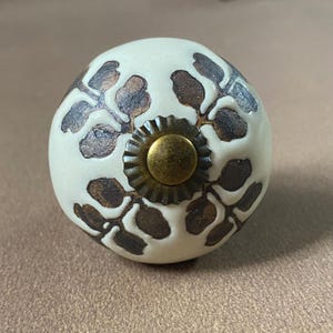 Puede incluir: Pomo de armario de cer&aacute;mica color crema con un dise&ntilde;o de hojas marrones. El pomo tiene un centro color lat&oacute;n y una base decorativa y estriada. Adecuado para cajones y armarios. Di&aacute;metro aproximado de 4 cm.