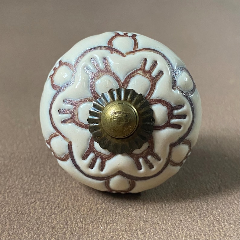 Puede incluir: Pomo de armario de cer&aacute;mica color crema con dise&ntilde;o floral marr&oacute;n. El pomo tiene una base de metal color lat&oacute;n y forma redondeada. Adecuado para cajones y armarios. Medidas en cent&iacute;metros.