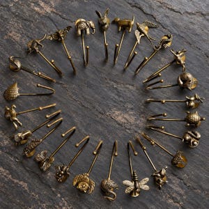 May include: A collection of antique brass-toned metal hooks arranged in a circle. Each hook features a unique animal or insect figure at the top, including an elephant, rabbit, bird, butterfly, bee, owl, turtle, squirrel, and various other creatures.