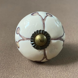 Puede incluir: Pomo de armario redondo de cer&aacute;mica blanquecina con dise&ntilde;o floral marr&oacute;n. El pomo presenta un centro color lat&oacute;n y una base de metal oscuro. Este herraje decorativo es adecuado para cajones y armarios.