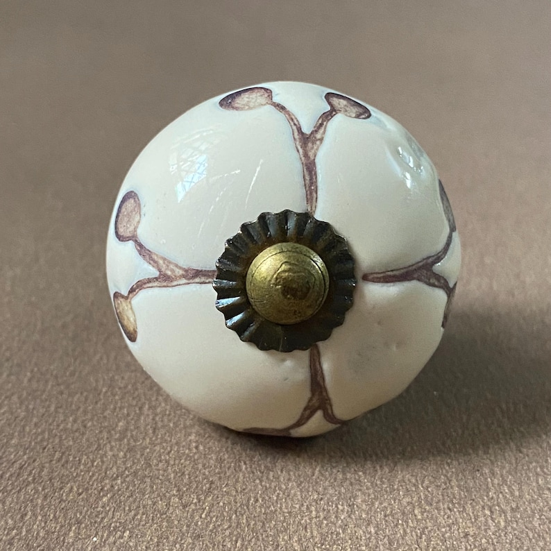Puede incluir: Pomo de armario redondo de cer&aacute;mica blanquecina con dise&ntilde;o floral marr&oacute;n. El pomo presenta un centro color lat&oacute;n y una base de metal oscuro. Este herraje decorativo es adecuado para cajones y armarios.