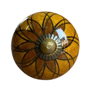 May include: A decorative cabinet knob with a floral design. The knob is a warm yellow colour with a brown floral pattern and a bronze-coloured metal base. The knob is round and has a glossy finish.