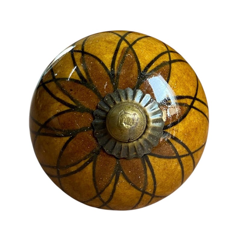 May include: A decorative cabinet knob with a floral design. The knob is a warm yellow colour with a brown floral pattern and a bronze-coloured metal base. The knob is round and has a glossy finish.