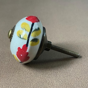 Puede incluir: Pomo de armario decorativo de cer&aacute;mica con dise&ntilde;o floral. El pomo es blanco con flores rojas y amarillas y hojas verdes. Tiene una base de metal y una varilla roscada para la instalaci&oacute;n.