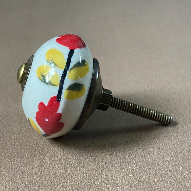 Puede incluir: Pomo de armario decorativo de cer&aacute;mica con dise&ntilde;o floral. El pomo es blanco con flores rojas y amarillas y hojas verdes. Tiene una base de metal y una varilla roscada para la instalaci&oacute;n.