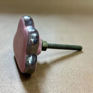 May include: A heart-shaped cabinet knob in light purple with a dark grey, shiny border. The knob has a threaded bolt and nut for fitting. The knob is suitable for use on drawers or cabinets.
