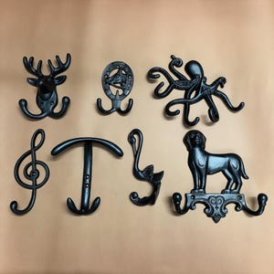 May include: Collection of black cast iron wall hooks in various designs, including a deer head, octopus, treble clef, and dog. The hooks are mounted on a neutral background, showcasing their decorative and functional nature.