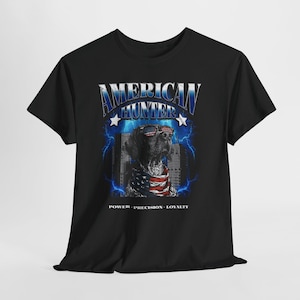 May include: Black t-shirt with a graphic of a dog wearing sunglasses and a bandana in the style of the American flag. The text "AMERICAN HUNTER" is in blue and silver, with "POWER - PRECISION - LOYALTY" below the dog.