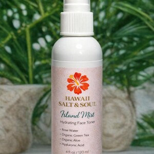 May include: White bottle of "Island Mist" hydrating face toner by Hawaii Salt & Soul. The label features a red and yellow hibiscus flower. The ingredients include rose water, organic green tea, organic aloe, and hyaluronic acid. The bottle contains 4 fl oz / 120 ml.