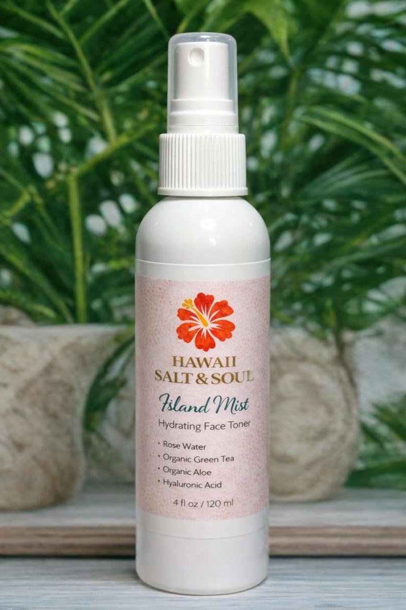 May include: White bottle of "Island Mist" hydrating face toner by Hawaii Salt & Soul. The label features a red and yellow hibiscus flower. The ingredients include rose water, organic green tea, organic aloe, and hyaluronic acid. The bottle contains 4 fl oz / 120 ml.