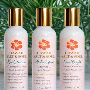 May include: Three white bottles of Hawaii Salt & Soul skincare products with gold caps and pink labels. Each label features an orange hibiscus flower and product name: Kai Cleanse, Aloha Glow, and Lani Bright. Each bottle contains 4 fl oz / 120 ml.