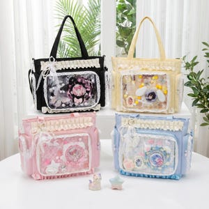 Könnte beinhalten: Vier Tragetaschen in Schwarz, Gelb, Rosa und Blau. Jede Tasche hat eine transparente Vordertasche mit dekorativen Gegenständen. Die Taschen haben Rüschenbesatz und Spitzenakzente. Die Taschen stehen auf einer weißen Oberfläche.