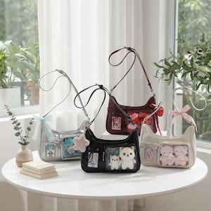 May include: Four shoulder bags in silver, black, burgundy, and cream, each with a unique design. The bags feature clear pockets displaying plush toys and character illustrations. Each bag has a long strap and is decorated with bows or charms.