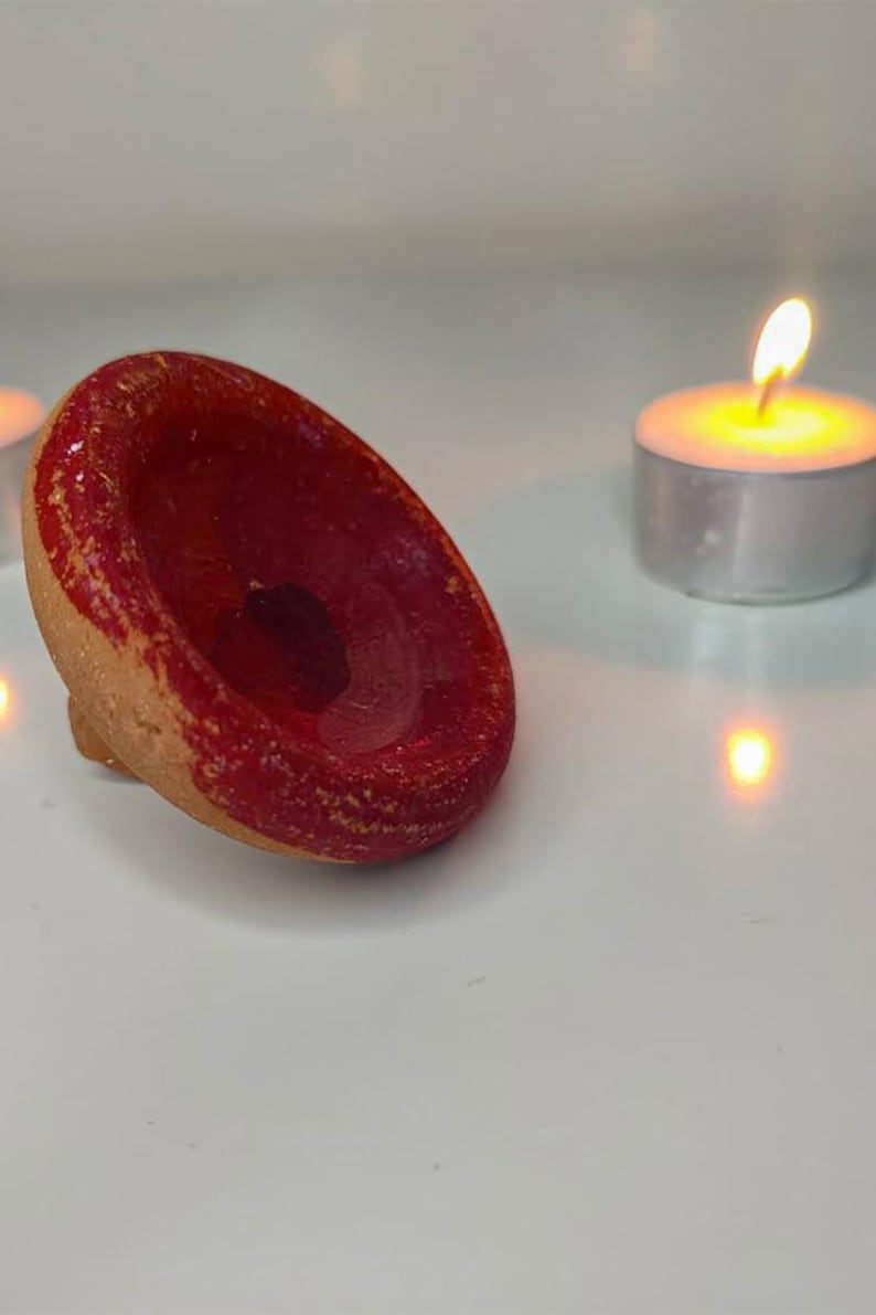 May include: A small, handmade ceramic bowl with a vibrant red interior and a natural, unglazed exterior. The bowl is set on a white surface, with a lit tea light candle in the background, creating a warm, inviting ambiance.
