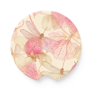 May include: A round car coaster with a botanical design featuring pink dragonflies, strawberries, and leaves. The background is a cream color, and the design has a watercolor effect. The coaster is made of absorbent material.