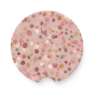 May include: Round car coaster with a blush pink background and a pattern of colorful, watercolor-style dots in shades of pink, gold, and brown. The coaster has a small notch for easy removal from the cup holder.