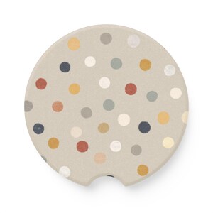 May include: A beige car coaster with a pattern of colorful polka dots in shades of red, yellow, blue, gray, and white. The coaster has a small notch on one side for easy removal from a car cup holder.
