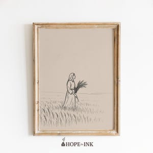 May include: A framed print featuring a minimalist line drawing of a person in a long dress carrying a bundle of wheat in a field. The artwork is in black and white, set against a beige background, and framed in a gold-toned wooden frame. The print is from "HOPE in INK".