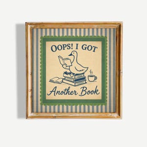 Può includere: Stampa incorniciata con un'anatra che legge un libro, con il testo "OOPS! I GOT Another Book". L'opera d'arte ha uno stile vintage, con un'anatra che legge un libro in cima a una pila di libri e una tazza di caffè. La cornice è dorata.