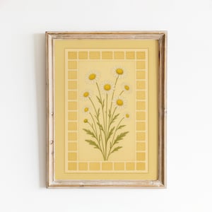 May include: A framed print featuring a bouquet of daisies. The daisies have white petals and yellow centers, set against a yellow background with a decorative border. The frame is a light, natural wood color.