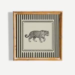 May include: A framed print featuring a black and white illustration of a leopard. The leopard is depicted walking on a light beige background, framed by a black and white striped border and a gold-colored frame.