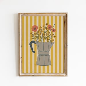 May include: Framed art print showing a grey stovetop espresso maker filled with flowers. The flowers are orange and yellow, set against a yellow and white striped background. The frame is a light wood colour.