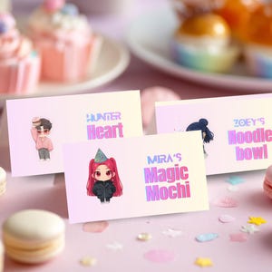 May include: Three pastel place cards with cartoon illustrations and text. The cards read "Hunter Heart," "Zoey's Noodle Bowl," and "Mira's Magic Mochi." The cards are on a pink surface with macarons and cupcakes in the background.