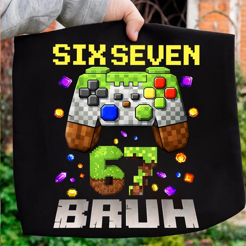 Op de afbeelding: Zwarte draagtas met een gepixeld videogamecontroller-ontwerp. De tekst "SIX SEVEN" staat bovenaan, met "67 BRUH" onderaan. De controller is groen, grijs, bruin, rood, geel en blauw, met kleurrijke gepixelde accenten.