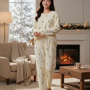 May include: Cream-colored pajama set with a repeating yellow pineapple pattern. The long-sleeved top and pants are made of a soft, textured fabric. The pajamas are designed for comfort and relaxation.